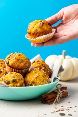 Pumpkin muffins with spices and seeds on plate. Women's hand takes muffin. Healthy sweet food. Blue background. Selective focus.