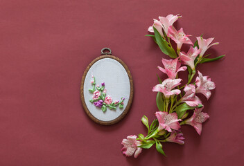 Spring needlework. Handmade gift for 8 March or birthday. Beautiful composition with alstroemeria flowers and floral embroidery with satin ribbons in hoop on brown background. Flat lay, copy space © Katvic