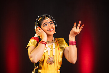 Enjoying indian bharatanatyam dancer listening favorite song on headphones at stage - concept of...