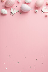 Top view vertical photo of easter decorations glowing confetti easter bunnies purple pink and white easter eggs on isolated pastel pink background with copyspace