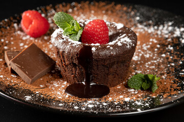 Small chocolate cake filled with liquid chocolate. Traditional French dessert coulant. Tasty hot cake melting chocolate syrup and decorated with cocoa powder, icing sugar, raspberries and mint.