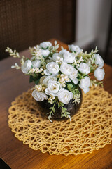 A bouquet of white artificial roses in a round brown pot stands on the table.