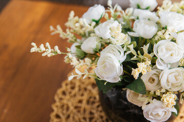 A bouquet of white artificial roses in a round brown pot stands on the table.
