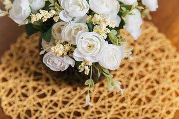 A bouquet of white artificial roses in a round brown pot stands on the table.
