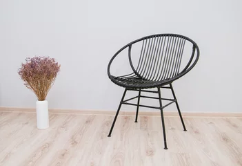 Fotobehang Wicker loft-style black chair against a white wall. Vase with dried flowers on the floor. © Вероника Преображенс