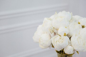 A bouquet of white artificial flowers stands in a vase against a white wall.