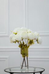 A bouquet of white artificial flowers stands in a vase against a white wall.