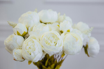 A bouquet of white artificial flowers stands in a vase against a white wall.