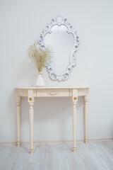 A bouquet of dry wildflowers stands in a white vase on a boudoir table by a vintage mirror.