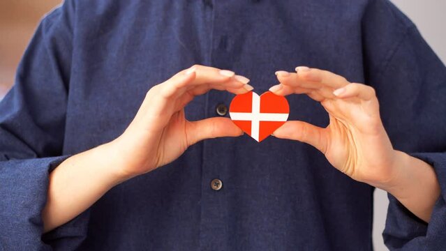 Young woman holds in her hands a heart in the form of a flag of Denmark. Patriotism concept. Love Denmark.
