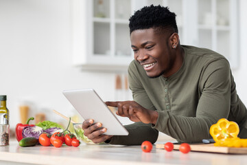 Fototapeta na wymiar Online Recipe. Smiling Black Guy Using Digital Tablet In Kitchen While Cooking