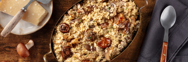 Mushroom risotto panorama with ingredients on a dark rustic wooden background, top shot