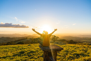Fototapeta na wymiar Teenager sitting on a wall enjoying a beautiful sunset with his hands raised. 