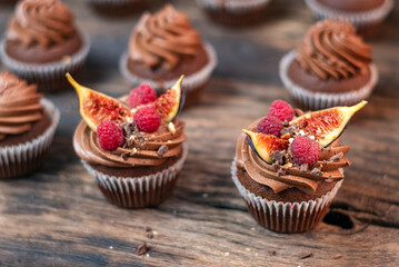 Delicious chocolate muffins with butter cream, raspberries and fig pieces. Coffee cupcakes on wooden table, close-up