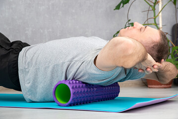Man doing myofascial release of hyper-flexible muscles of back with massage foam roller....