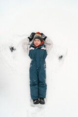 Fototapeta na wymiar Happy child boy playing on winter in the snow. Kid making snow angel. Top view. Vertical frame.
