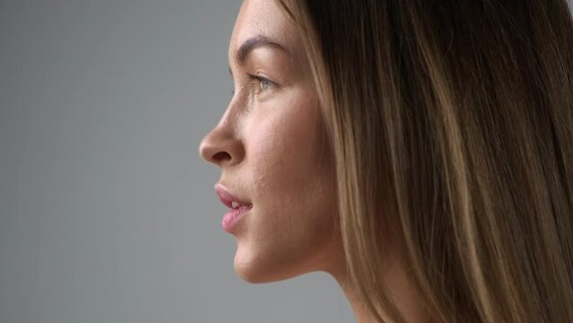 Beauty face of a young blonde woman in profile close-up. Smile, beautiful eyes, lips and teeth. Grey background