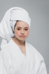 Young woman with down syndrome in towel and bathrobe looking at camera isolated on grey