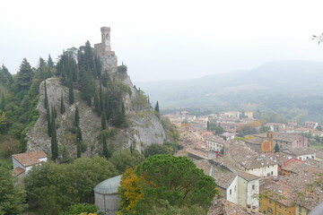 panorama of the clock tower in Brisighella surrounded by the green countryside on a hill that...