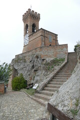 clock tower in Brisighella with mighty brick walls and the clock face at six hours on a hill that...