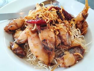 Seafood menu called Deep Fried Squid with Tamarind Sauce and crispy fried rice noodles served on a white plate with a stainless steel spoon placed on the side. Sweet and sour taste, eat with hot rice.