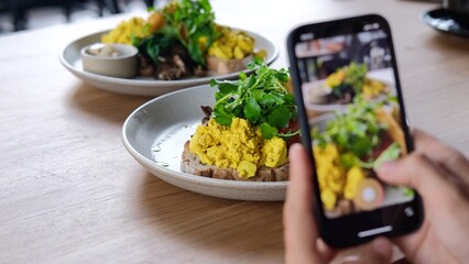Lifestyle blogger tacking videos and photos of fresh morning toasts with scrambled eggs for social media content in a cafe