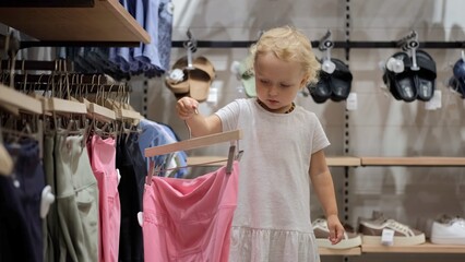 Adorable cute small toddler girl choosing a stylish outfit in a clothing store, shopping fashion apparel