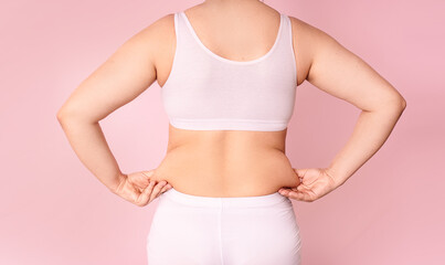 A young woman pinches fat on the side of her waist to show a flabby, overweight body after pregnancy and childbirth.