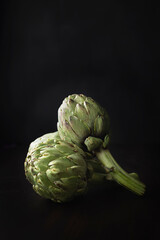 Fototapeta premium Fresh and raw artichokes on a dark background with space for text