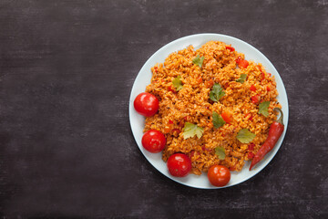 Jollof rice, tomatoes and hot peppers on a blue plate, fork, spoon on a linen napkin on a black background. National cuisine of Africa.