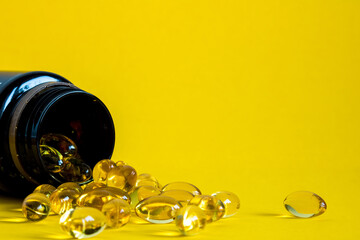 a jar lies on its side with omega 3 capsules on a yellow background, copyspace, scattered