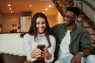 Caucasian female sitting with African American boyfriend while texting on cellular device relaxing on sofa