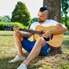Summer portrait of young man plying guitar outdoor