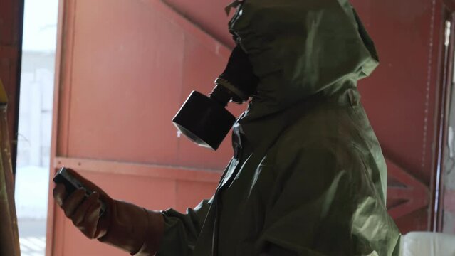 Silhouette faceless person in green defensive cloak dialing with radiometer. Radiation danger concept.