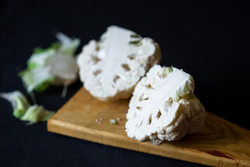 Cut cauliflower in half on a cutting board. Dark background. Cooking cauliflower steak. Vegetarian food, diet concept.