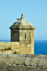 A seagull sits on a castle tower of castillo de Santa B&aacute;rbara in Alicante overlooking the Mediterranean Sea under clear blue sky