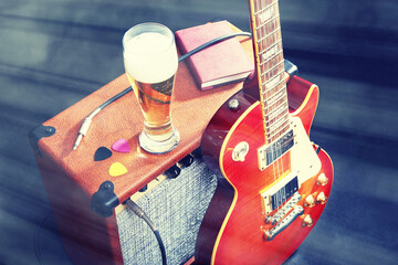 Guitar combo amplifier with guitar, glass of beer and notepad on black background. Gently toned.