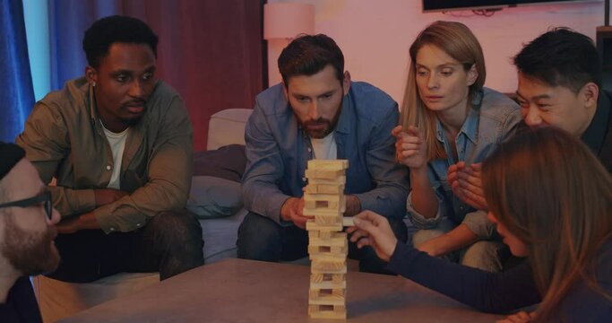 Big Company of Men and Girls playing Game with Wooden Blocks at Home. Sitting on the sofa playing Jenga Building Tower smiling and Spending Time Together. The concept of Relaxation and Entertainment.