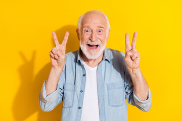 Portrait of attractive cheerful grey-haired man showing double v-sign having fun isolated over...