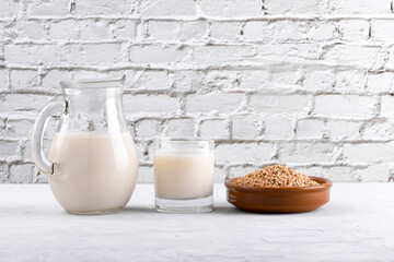 Vegan non diary buckwheat milk in jug and glass with buckwheat groats a bowl on a white stone table. Vegan buckwheat drink is plant based alternative milk . Veggies healthy milk product in pitcher