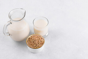 Vegan non diary buckwheat milk in jug and glass with buckwheat groats a bowl on a white stone table. Vegan buckwheat drink is plant based alternative milk . Veggies healthy milk product in pitcher