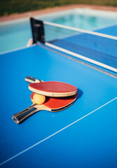 Close up of ping pong or table tennis rackets near a swimming pool. Summer and vacation concept.