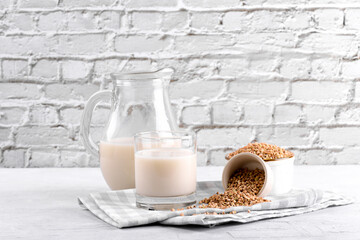 Vegan non diary buckwheat milk in jug and glass with buckwheat groats a bowl on a white stone table. Vegan buckwheat drink is plant based alternative milk . Veggies healthy milk product in pitcher