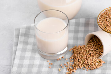 Vegan non diary buckwheat milk in glass with buckwheat groats in a bowl and on white stone table. Vegan buckwheat drink is plant based alternative milk . Veggies healthy milk product, selective focus