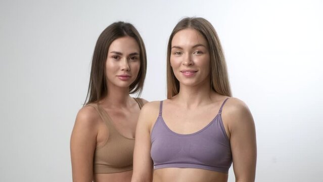 Two young multiracial women, asian and a caucasian girls, pose together on a white background. Beautiful bodies and perfect skin, cotton underwear.