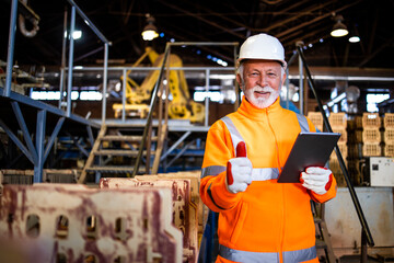 Portrait of an industrial employee standing by production machines an holding thumbs up for successful results.