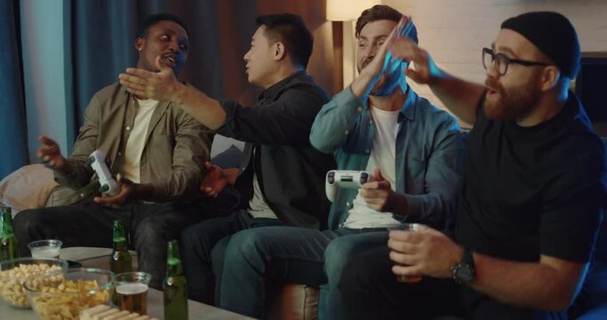 Happy Company of Man having fun while Playing Video Games at Home and Win. Group of Adult Men sitting in living room with Drinks and Snacks holding Joysticks. Technology. Entertainment. Temaplay