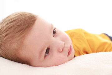  The 3-year-old sits on a fluffy white blanket in a white room and looks around. © marindumitru