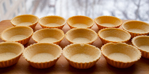 Tartlets made of dough lie on a wooden board. On the background of the window. Panorama.