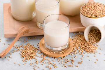Vegan non diary buckwheat milk in glasses with buckwheat groats in a bowl on white stone table....